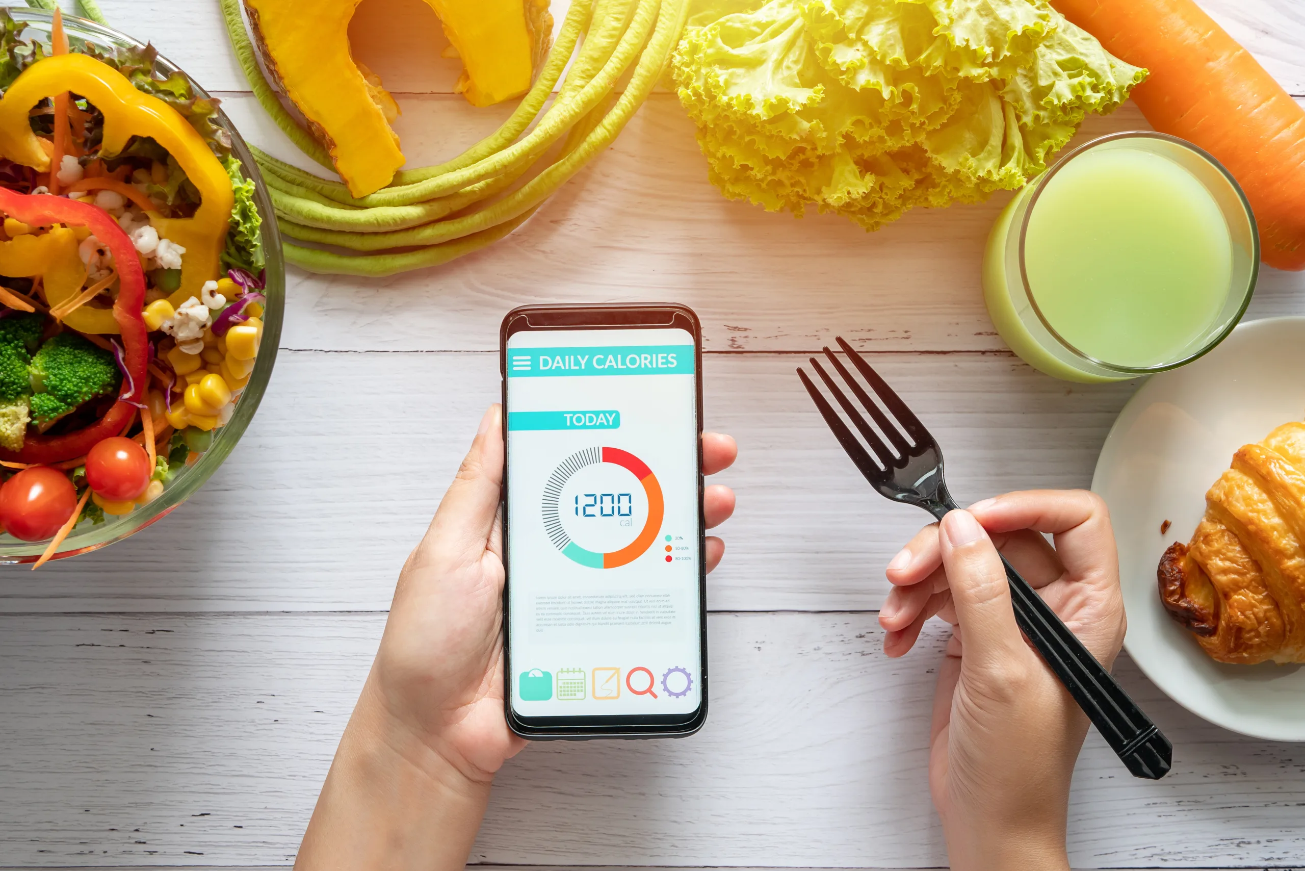 Calories counting , diet , food control and weight loss concept. woman using Calorie counter application on her smartphone at dining table with salad, fruit juice, bread and vegetable - 神楽坂・飯田橋で人気のパーソナルジム|QUALITAS神楽坂店【トレーニング×痩身エステ】 女性がスマホで食事指導を受けている様子