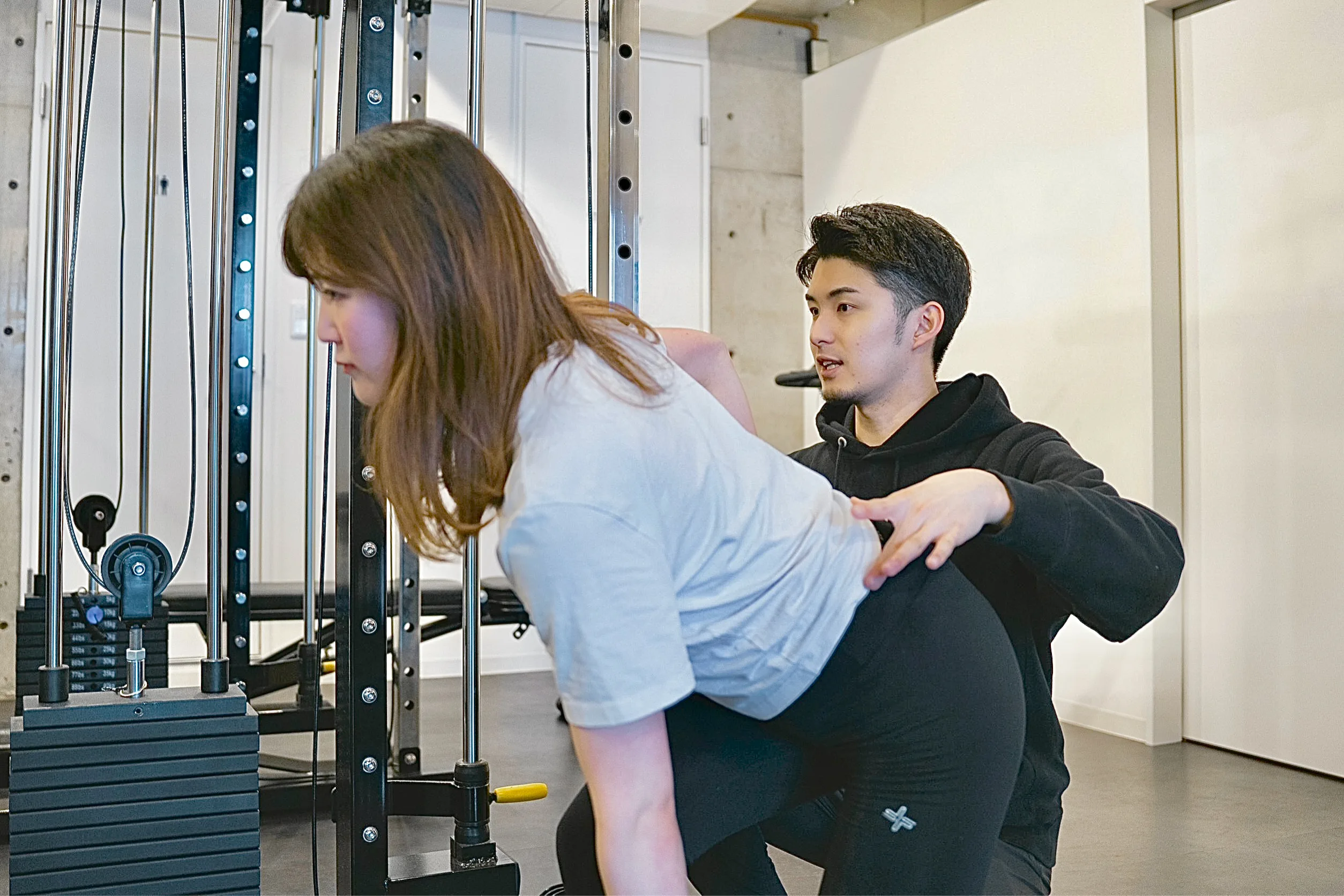 名称未設定-1 - 神楽坂・飯田橋で人気のパーソナルジム|QUALITAS神楽坂店【トレーニング×痩身エステ】 パーソナルジムQUALITAS神楽坂店で男性トレーナーにトレーニング指導を受けている女性